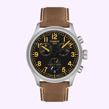 A Tissot Watches Chrono L 42mm T1164171605201 by Tissot Watches, featuring a brown leather strap, black dial with yellow-orange numerals, three sub-dials, Swiss Quartz chronograph movement, and a scratch-resistant sapphire crystal—photographed against a light purple background.