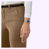 A person wearing tan pants, a white long-sleeve shirt, and the Tissot Watches Classic Dream 28mm T1292101105300 by Tissot Watches stands with their arm by their side against a light lavender background.