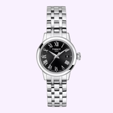 The Tissot Watches Classic Dream 28mm T1292101105300, a women’s stainless steel wristwatch by Tissot Watches, features a black dial with Roman numerals, silver hands, a date window at 3 o’clock, and a sleek metal link bracelet. Displayed against a pale lilac background, this elegant timepiece highlights Swiss quartz precision and timeless design.