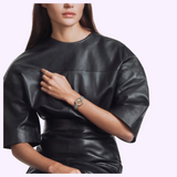 A woman wears a Tissot Watches Desir 29.6mm T1522231154600 watch with a round, gold-accented face and a metallic link bracelet on her wrist.