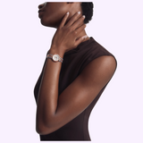 A person wearing a silver and rose gold-tone Tissot Watches Desir 29.6mm T1522232203600 watch with a white dial and diamond hour markers on their wrist.