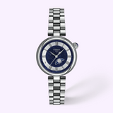 Tissot Watches Desir T1522231149300 in silver-tone stainless steel, featuring a round, dark blue glitter dial with silver Roman numerals, a moon phase display, and a metallic link bracelet.