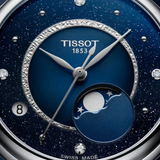Close-up of a Tissot Watches Desir T1522231149600 watch face featuring a glittery blue finish, silver hands, a moon phase display, diamond hour markers, and a date window.