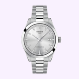 The Tissot Watches Gentleman 38mm T1658071103100 features a stainless steel band, minimalist silver dial with date at 3 o’clock, and Powermatic 80 text, displayed against a light purple background.