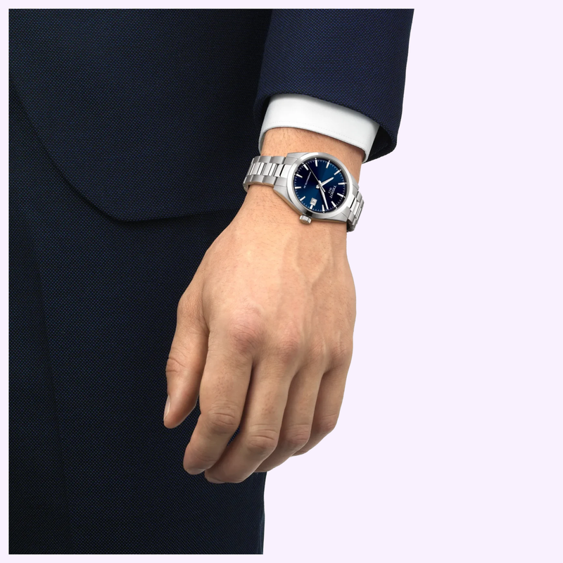 Person in a dark blue suit and white shirt wearing the Tissot Gentleman 38mm T1658071104100 with blue dial on their left wrist