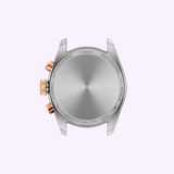 Back view of a Tissot Watches PR 100 36mm T1502172211100 stainless steel case, featuring rose gold crown and pushers, engraved with water resistance information, sapphire crystal details, and model numbers, set against a light purple background.