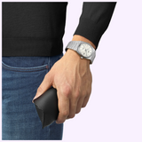 A person wearing a Tissot Watches PRX 40mm T1374071111100 watch with a white textured dial and a metal link bracelet on their wrist.