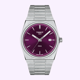 The Tissot Watches PRX 40mm T1374101140100 from Tissot Watches features a stainless steel band and a vibrant purple dial accented with silver hour markers and a date window at 3 o’clock, elegantly displayed against a light background.