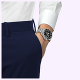 A person wearing navy blue pants, a white dress shirt, and a Tissot Watches Seastar 2000 44mm T1209071105100—featuring Swiss automatic movement and a black face—has one hand in their pocket.