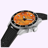 The Tissot Watches Seastar 2000 44mm T1209071728100 features an orange dial, black textured rubber strap, silver case, black unidirectional bezel, and white hour markers, shown against a light purple background.