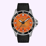 The Tissot Watches Seastar 2000 44mm T1209071728100 features an orange dial, black bezel, black textured strap, Swiss automatic movement, white hour markers, black hands, and a date window at 6 o’clock.