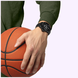 A person wearing a dark green sweatshirt and a Tissot Watches Seastar 2000 44mm T1209073705100 on their wrist holds an orange basketball against a light background.