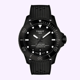 The Tissot Watches Seastar 2000 44mm T1209073705100 by Tissot Watches is a professional dive watch in black, featuring a wave-patterned dial with luminous markers, a black rotating bezel, and a black textured strap. It is powered by the reliable Powermatic 80 Swiss automatic movement and is displayed against a light purple background.