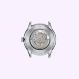 Back view of the Tissot Watches Seastar Chemin Des Tourelles Skeleton 39mm (T1398361626100) in silver, showcasing its exposed inner gears and intricate Swiss automatic movement, set against a light purple background.