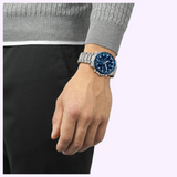 A man wearing a 42mm Tissot Watches Supersport Chrono T1254171104100 with a blue dial and a stainless steel metal link bracelet on his wrist.