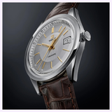 The Tissot Watches Visodate 39mm T1574071603100 by Tissot Watches, featuring a silver case, brown leather strap, gold hour markers, and a date display, is displayed at an angle on a dark background.