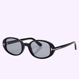 Tom Ford Sunglasses FT1364/s 4901A in black, featuring oval frames with dark lenses, elegant gold accents on the temples, and a discreet Tom Ford logo on the upper corner of the right lens, are displayed against a light lavender backdrop—an ideal accessory to add Miami chic to any outfit.