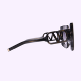 Side view of the Valentino Sunglasses V - SOUL VLS-127A-53 for women in black, featuring thick frames and a bold “V” shaped metal accent on the arm, showcased against a light purple background—an ideal choice for those seeking chic, Miami-inspired flair.