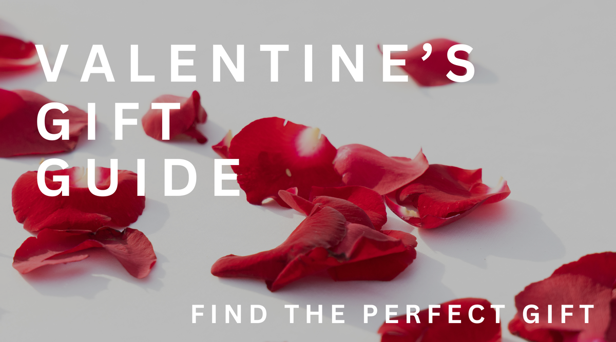 Red rose petals scattered on a white surface with large text reading Valentines Gift Guide and smaller text below saying Find the perfect gift.