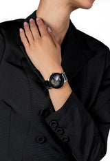 A person in a black blazer touches their neck, showcasing a Rado Watches R30012152 Centrix Automatic Open Heart wristwatch with a metallic band, open-heart dial, visible gears, and an antimagnetic Nivachron hairspring.