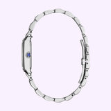 The Citizen Watches Citizen L Bianca EW5620-55A, a silver women’s luxury wristwatch by Citizen Watches, is pictured from the side with its metallic band forming an oval shape and featuring a blue gem on the crown, set against a light purple background—an elegant accessory crafted for timeless sophistication.