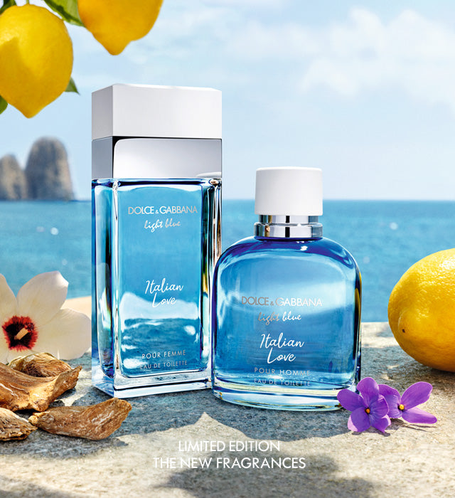 Two bottles of Dolce & Gabbana Light Blue Italian Love fragrance are displayed on a stone surface with lemons, flowers, and a scenic coastal backdrop. Text at the bottom reads Limited Edition, The New Fragrances.