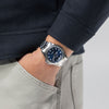 A person in a navy jacket and light gray pants stands with a hand in their pocket, showing off the Hamilton Watches Khaki Field King Day-Date 40mm H64475140—a sleek timepiece from Hamilton Watches, ideal for Miami style.