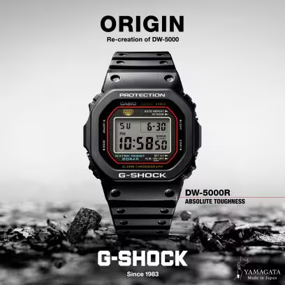 A CASIO G-Shock Watch DIGITAL DW5000R-1A by G-Shock Watches sits atop scattered black rocks, displaying 10:58:50. Text reads “ORIGIN,” “Re-creation of DW-5000,” “40th Anniversary,” and “Absolute Toughness.”.available at lexor miami