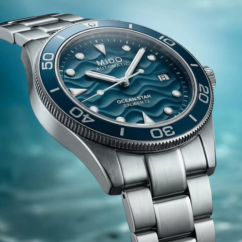 Close-up of Mido Ocean Star 39 blue wave-patterned dial with date display and silver hour markers over an underwater background