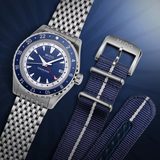 The Mido Watches OCEAN STAR GMT M0268291804100 features a blue and white dial, blue bezel, metal bracelet, plus two extra blue fabric straps, displayed on a striking blue radial background.
