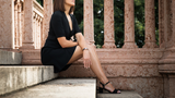 A woman in a black dress and sandals sits on stone steps by a pink marble railing, wearing the Frederique Constant Classics Slimline Ladies Moonphase FC-206MPWD1S2B watch; greenery frames the background.