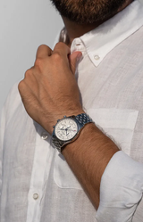 A man in a white button-up shirt adjusts his collar, revealing a Frederique Constant Classics Quartz Chronograph Triple Calendar FC-296SW5B6B watch with a white dial and metal band on his left wrist.