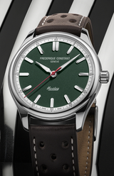 A close-up of the Frederique Constant Vintage Rally Healey Automatic FC-301HGRS5B26 men's watch with a racing green dial, silver markers, red seconds hand, and a brown perforated leather strap on a shiny black and white striped surface.