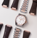 The Frederique Constant Highlife Automatic COSC FC-303V4NH2B, a Swiss watch with a white face and rose gold accents, is displayed with interchangeable leather, metal, and fabric straps on a light surface.