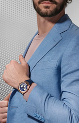 A man in a light blue textured suit jacket and pale pink shirt showcases the Frederique Constant Watches Highlife Chronograph Automatic FC-391NS4NH4. His neatly groomed beard is partially visible as he displays the striking Swiss timepiece.