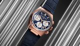 The Frederique Constant Highlife Chronograph Automatic FC-391NS4NH4 watch, featuring a rose gold case, blue dial with white subdials, and blue textured strap, is displayed between angled metallic rods, reflecting Swiss luxury craftsmanship.