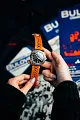 A person holds a Bulova Watches Chronograph A 98B427 Men with an orange band and detailed round face. Blue and white bull-themed cards stand out in the background—ideal for fans of this striking Bulova timepiece.