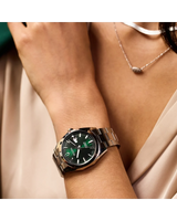 A person wears the Bulova Watches Surveyor 96B429 men’s watch, featuring a stainless steel band, green dial, and white indices, paired with a light blouse and a silver oval pendant necklace.