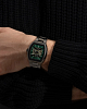 A person in a dark textured sweater, arms crossed, wears a Bulova Watches Maquina 98A321 with a black and green dial on their left wrist.