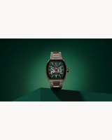 A stylish Bulova Maquina 98A321 wristwatch by Bulova Watches, featuring a green face and intricate pattern, stands upright on a geometric green surface against a dark green gradient backdrop.