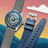The Mido Watches SPECIAL EDITION OCEAN STAR DECOMPRESSION WORLDTIMER M026.829.17.041.00 men's watch, with a blue multicolored dial and silver mesh strap, is shown beside an extra blue rubber strap against a vibrant abstract ocean-inspired background.