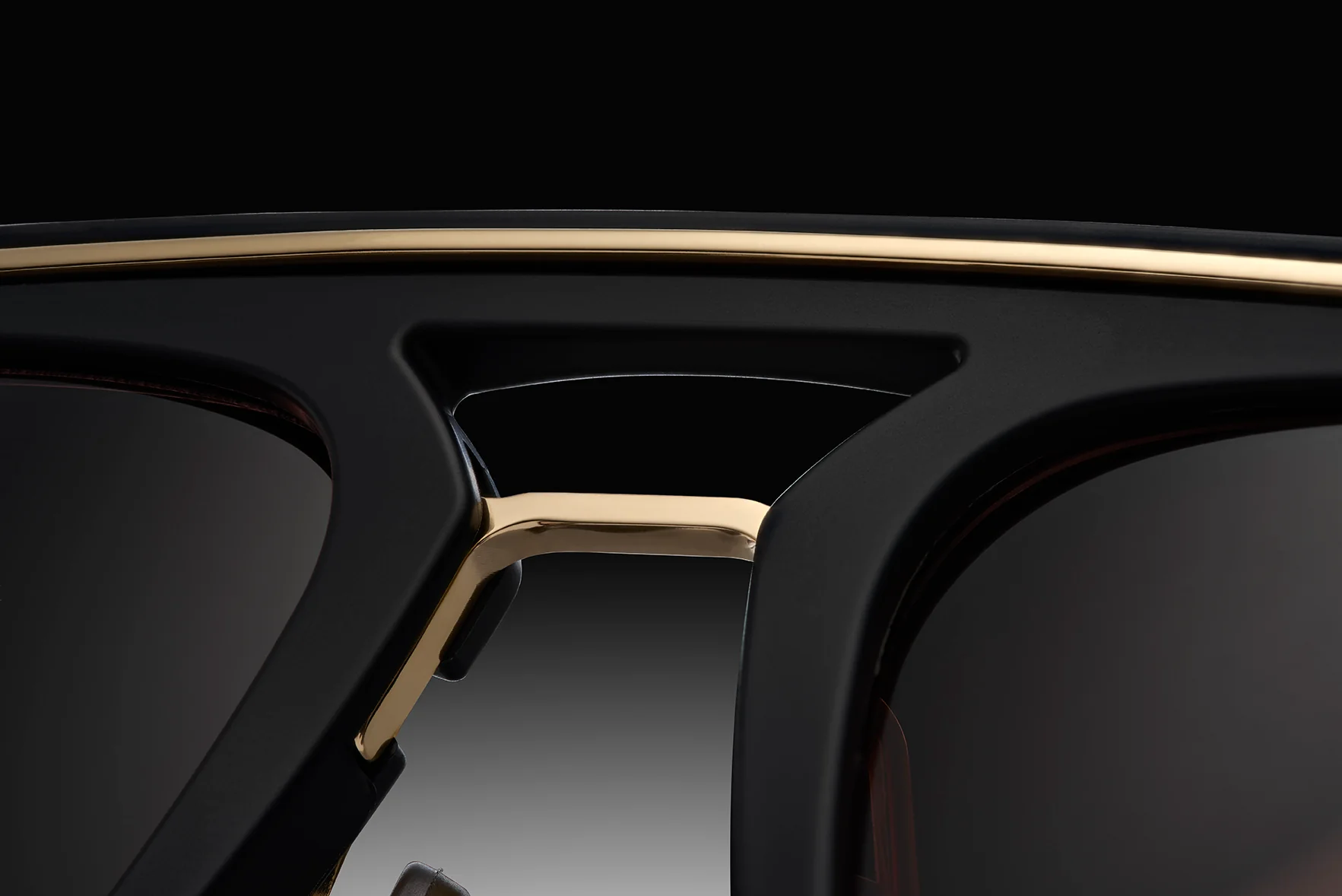 Close-up of the bridge and top rim of Dita Sunglasses DLS404-56-02-A LSA-404 by Dita Sunglasses, featuring gold accents, a bold black frame, and dark polarized lenses against a gradient black background.
