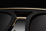 Close-up of the bridge and top rim of Dita Sunglasses DLS404-56-02-A LSA-404 by Dita Sunglasses, featuring gold accents, a bold black frame, and dark polarized lenses against a gradient black background.