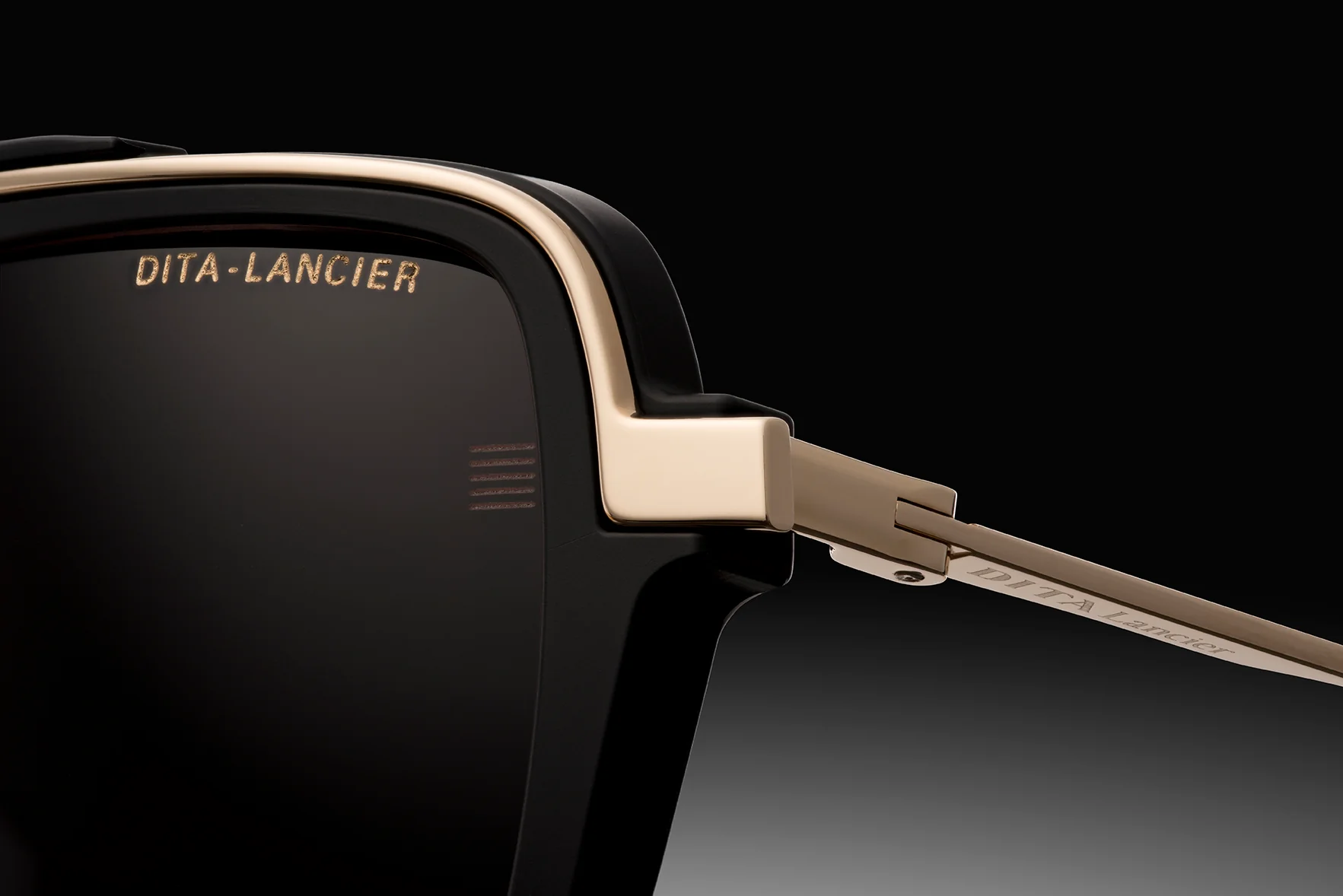 Close-up of Dita Sunglasses DLS404-56-02-A LSA-404 by Dita Sunglasses, featuring high contrast black frames, gold accents, and the logo engraved on polarized lenses and temple arm. Background transitions from deep black to gray.