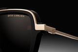 Close-up of Dita Sunglasses DLS404-56-02-A LSA-404 by Dita Sunglasses, featuring high contrast black frames, gold accents, and the logo engraved on polarized lenses and temple arm. Background transitions from deep black to gray.