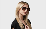 A woman with straight blonde hair wears large, square, unisex Dita Sunglasses DUBSIGNAL DTS465-A-03 (UPC 0810121956724) and a black top while posing against a plain light gray background.