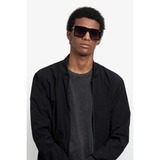 A person wearing Carrera Sunglasses VICTORY C 07/S 7C5 (UPC: 197737059095), a black jacket, and a dark t-shirt stands against a plain white background with a neutral expression.