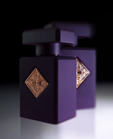 Two elegant dark purple bottles of Initio Parfums Prives Side Effect 3.0 oz EDP Perfume by Initio Perfumes, adorned with gold ornate diamond-shaped labels and placed side by side on a glossy surface against a black background, capture the allure of luxury and evoke the sophisticated tobacco-vanilla essence of this exclusive fragrance.