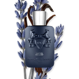 A dark blue bottle of Parfums de Marly Layton 4.2oz EDP Man Perfume by Parfums De Marly Perfumes is displayed among lavender flowers and vanilla beans on a light background, reflecting the elegant oriental floral character of this distinguished men’s fragrance.