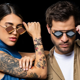 A woman with a tiger tattoo on her arm and a man pose confidently against a black background, both wearing Vysen Jaxs J-6 Unisex Sunglasses by Vysen Sunglasses. Handcrafted in Italy, these frames lend an air of sophistication to their modern style.